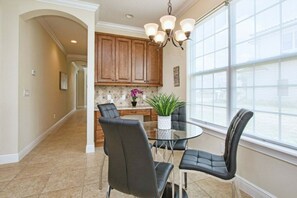 A dining area with a round table, four chairs, a chandelier, and a view of the kitchen. - 5BR Reunion home | Pool, spa & Disney rooms (Kissimmee)