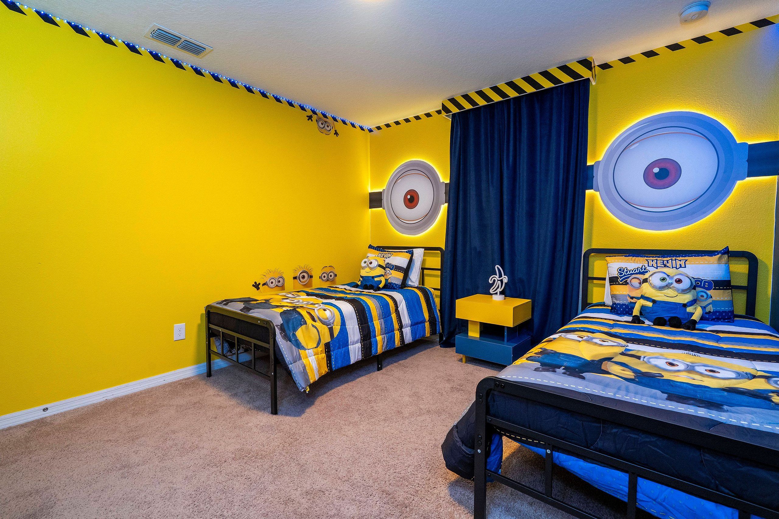 A bedroom with two beds, each with a Minion-themed duvet, a nightstand with a lamp, and a wall with circular light fixtures.