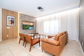 Ein modernes Wohnzimmer mit Sofa, Sesseln, Fernseher und Essbereich.