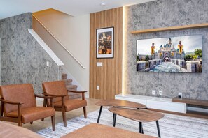 Un salon moderne avec un escalier, des fauteuils en cuir, un téléviseur à écran plat et un tapis à motifs.