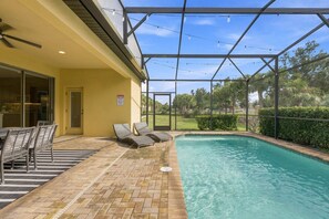 Ein Poolbereich mit Glasveranda, Liegestühlen und einer Pflasterterrasse.