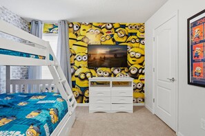 Ett sovrum med våningssängar, en byrå och en vägg med en tapet med Minion-motiv.