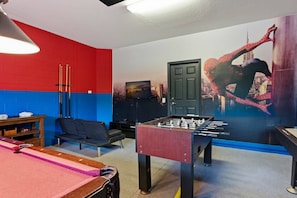 Ein Zimmer mit einem Kicker, einem Fernseher, einer Couch und einem Wandgemälde.