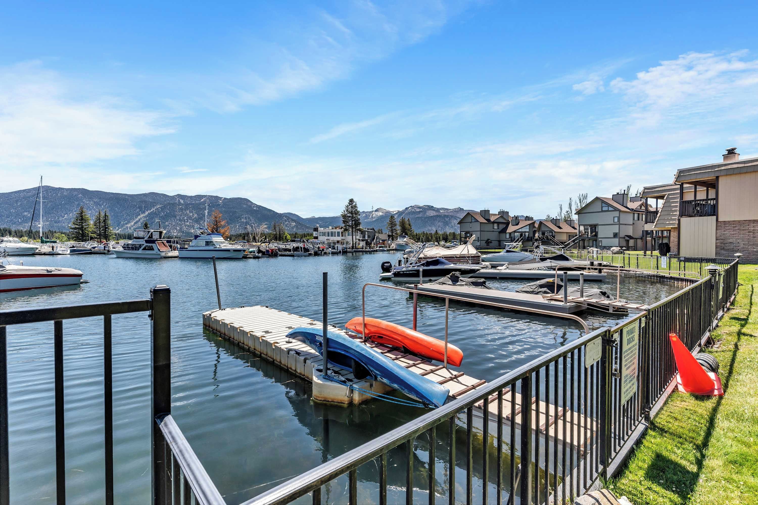 Un puerto deportivo con barcos amarrados, un muelle con kayaks y casas al fondo.