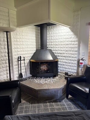 Una habitación de esquina con chimenea de piedra, un sillón de cuero negro y un extintor en la pared.