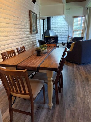 Un comedor con una mesa y sillas de madera, chimenea y pared de piedra.