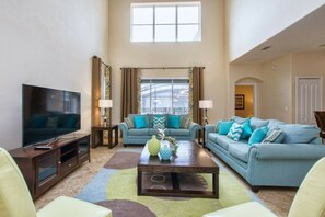 A living room with a television, two sofas, a coffee table, and a large window. - 5BR home near Disney | Pool & Mickey room (Kissimmee)