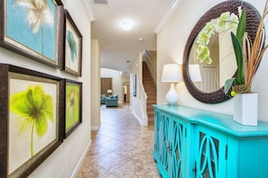 A hallway with framed artwork, a teal console with a mirror, and a staircase leading to another room. - 5BR home near Disney | Pool & Mickey room (Kissimmee)