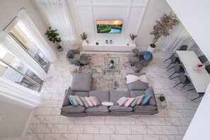 A spacious living room with a large gray sectional sofa, a coffee table, and a flat-screen TV mounted on the wall. - 5BR ChampionsGate | Cinema, themed rooms, pool (Davenport)