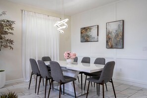 A modern dining area with a white table, grey chairs, a hanging light fixture, and two abstract paintings on the wall. - 5BR ChampionsGate | Cinema, themed rooms, pool (Davenport)