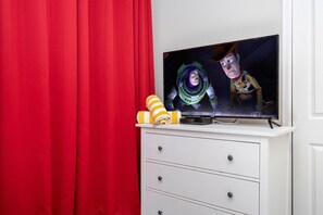 En tv-apparat står på ett vitt skåp, och i bakgrunden hänger en röd gardin.