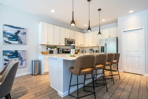 A modern kitchen with white cabinets, a central island with bar stools, stainless steel appliances, and pendant lighting. - 6BR Sonoma Resort home | Pool & Cars game room (Kissimmee)