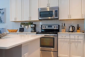 A modern kitchen with stainless steel appliances, white cabinetry, and a built-in oven. - 6BR Sonoma Resort home | Pool & Cars game room (Kissimmee)