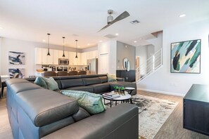 A modern living room with a sectional sofa, a coffee table, and a dining area in the background. - 6BR Sonoma Resort home | Pool & Cars game room (Kissimmee)