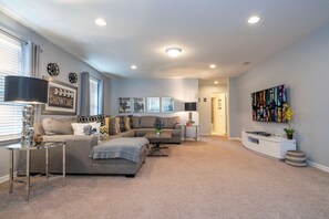 A living room with a sectional sofa, a coffee table, and a flat-screen TV mounted on the wall. - 6BR near Disney | Private pool, spa, movie room (Kissimmee)