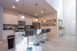 A modern kitchen with a central island, bar stools, and pendant lighting. - 6BR near Disney | Private pool, spa, movie room (Kissimmee)