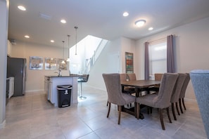 A modern kitchen with a dining area, a trash bin, and a staircase leading to another level. - 6BR near Disney | Private pool, spa, movie room (Kissimmee)