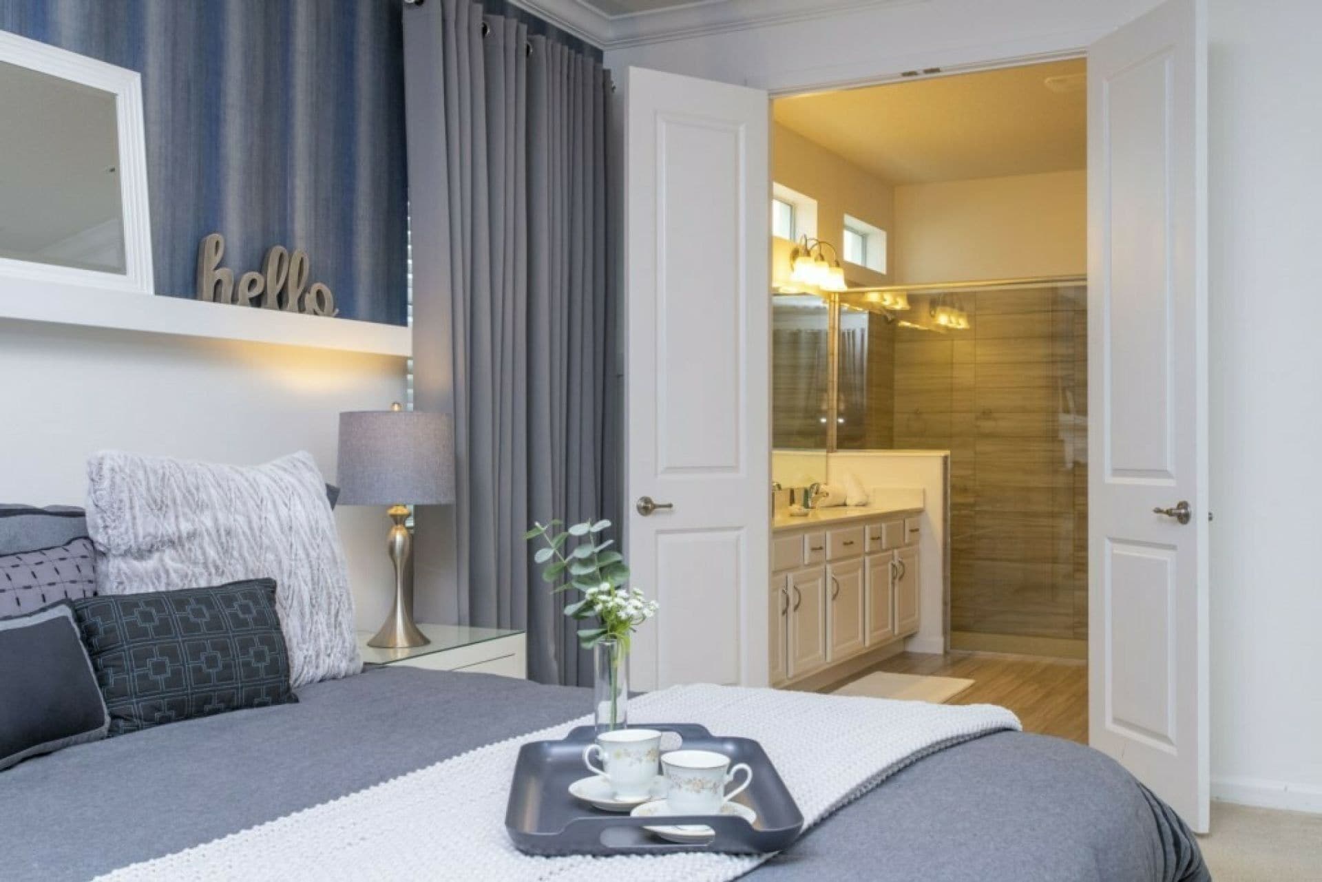 Une chambre à coucher avec un lit, une table de chevet, une lampe et un plateau avec des tasses et des soucoupes.