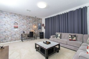 Olohuone, jossa on sohva, sohvapöytä, työpöytä ja seinä, jossa on julisteita.
