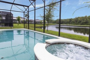 A swimming pool with a hot tub, surrounded by a glass enclosure with a view of a lake and houses. - 6BR near Disney | Pool, spa, Mickey & Marvel (Kissimmee)