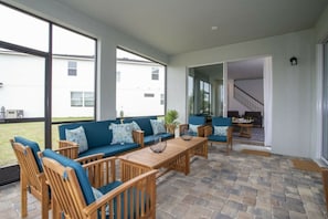 A covered patio area with a sofa set, wooden chairs, and a table. - 6BR Solara Resort | Pool, spa & game room (Kissimmee)