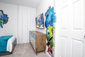 A bedroom with a bed, a wooden dresser, a TV, and a wall with a cartoon character. - 6BR Solara Resort | Pool, spa & game room (Kissimmee)