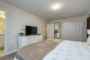 Quarto com cama, televisão sobre um penteadeira e guarda-roupa.