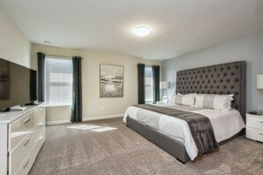 A hotel room with a bed, a television, a desk, and a window with curtains. - Storey Lake 6BR | Lego & Mickey rooms, pool (Kissimmee)