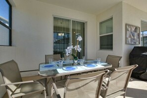A patio with a glass table set for four, surrounded by wicker chairs. - Storey Lake 6BR | Lego & Mickey rooms, pool (Kissimmee)