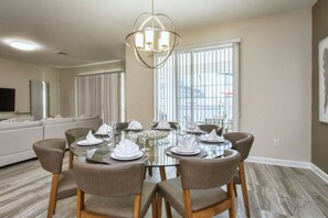 A dining area with a round glass table, six chairs, and a chandelier. - Storey Lake 6BR | Lego & Mickey rooms, pool (Kissimmee)