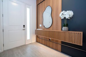 Un interior modern amb una porta blanca, un panell de fusta, un mirall gran i una orquídia en test.