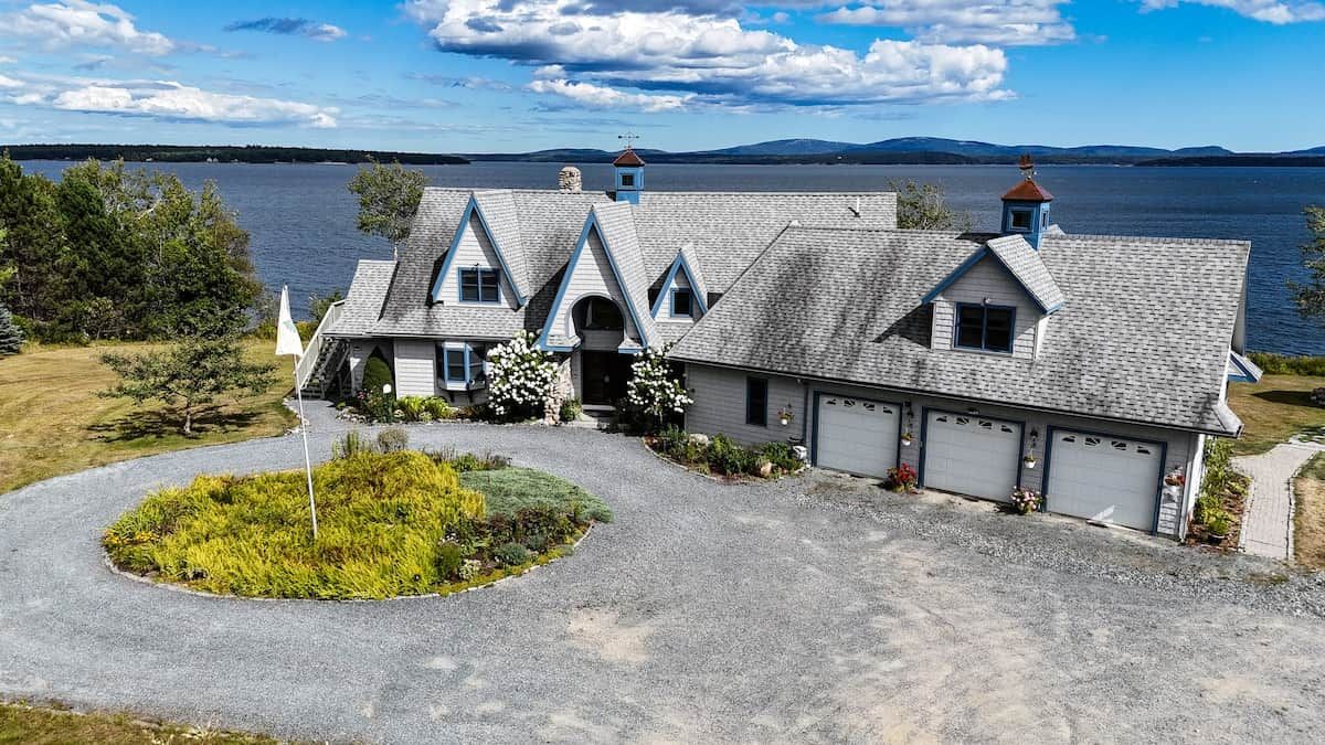 A two-story house with a steeply pitched roof, a garage, and a driveway leading to a landscaped area with a circular garden.