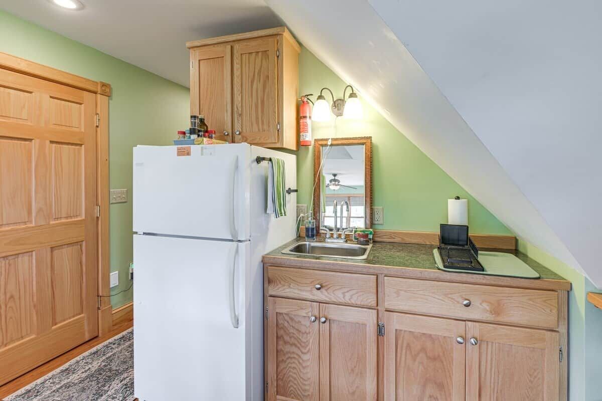 A compact kitchen with wooden cabinets, a white refrigerator, a sink, and a mirror above the countertop.