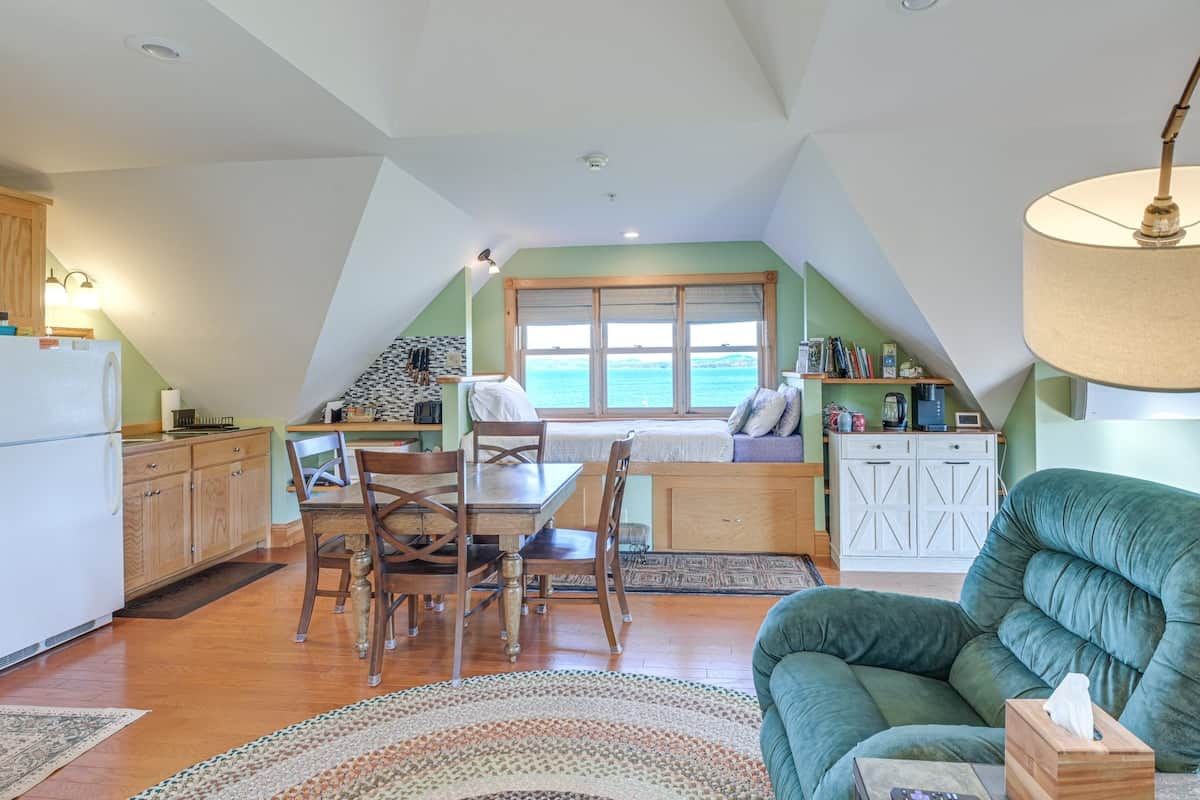 A cozy interior with a dining area, kitchen, and a large window overlooking the sea.
