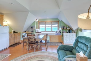 A cozy interior with a dining area, kitchen, and a large window overlooking the sea. - Peaceful Loft with Gazebo and Firepit (Surry)