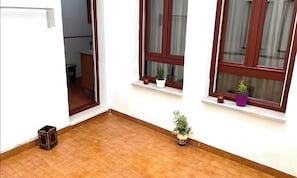 Una habitació amb terra de rajola, una finestra amb cortina i una petita planta en test amb pal·la a la finestra.