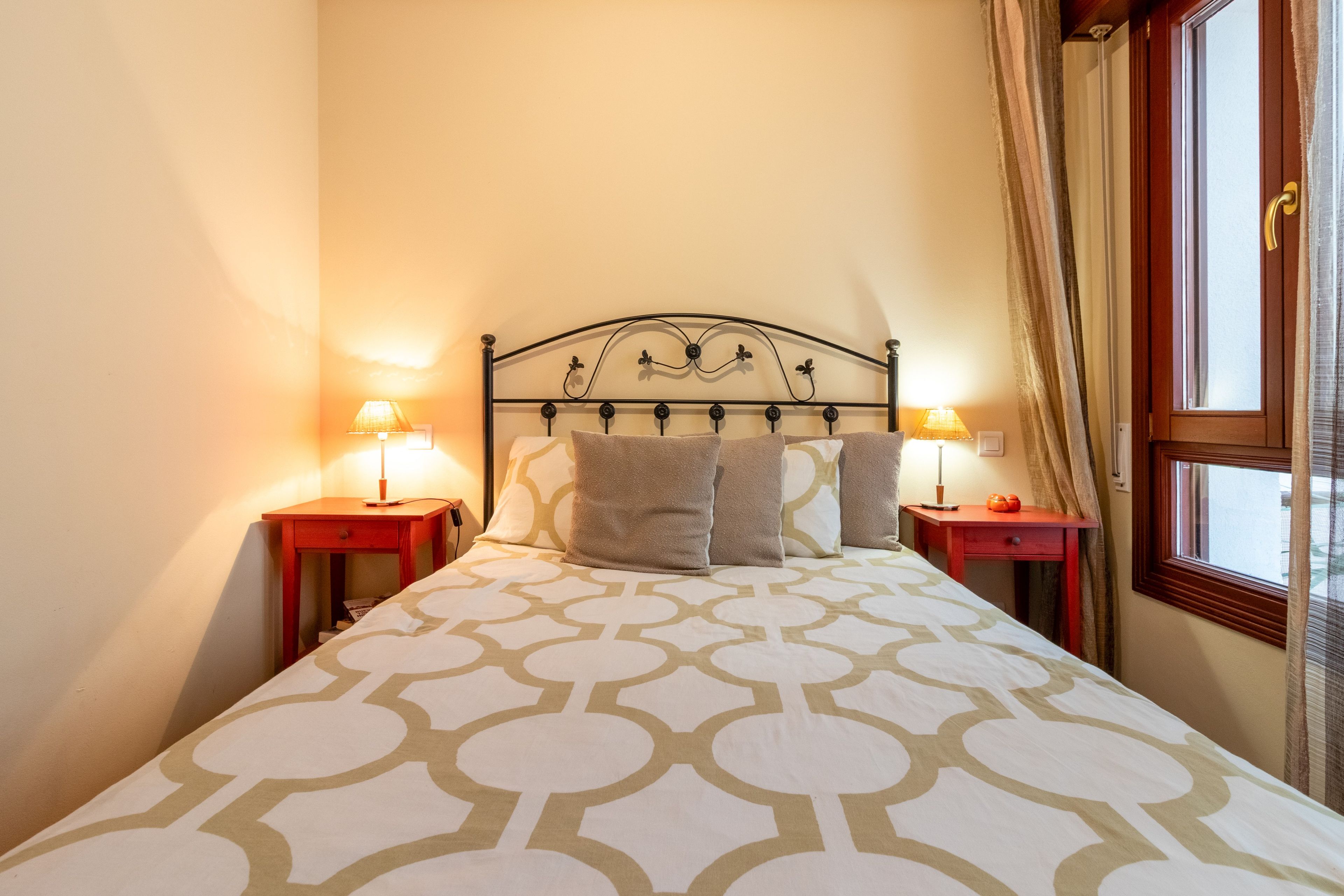 Un letto rifatto con cura, un copriletto decorato, due comodini con lampade e una finestra con tende.