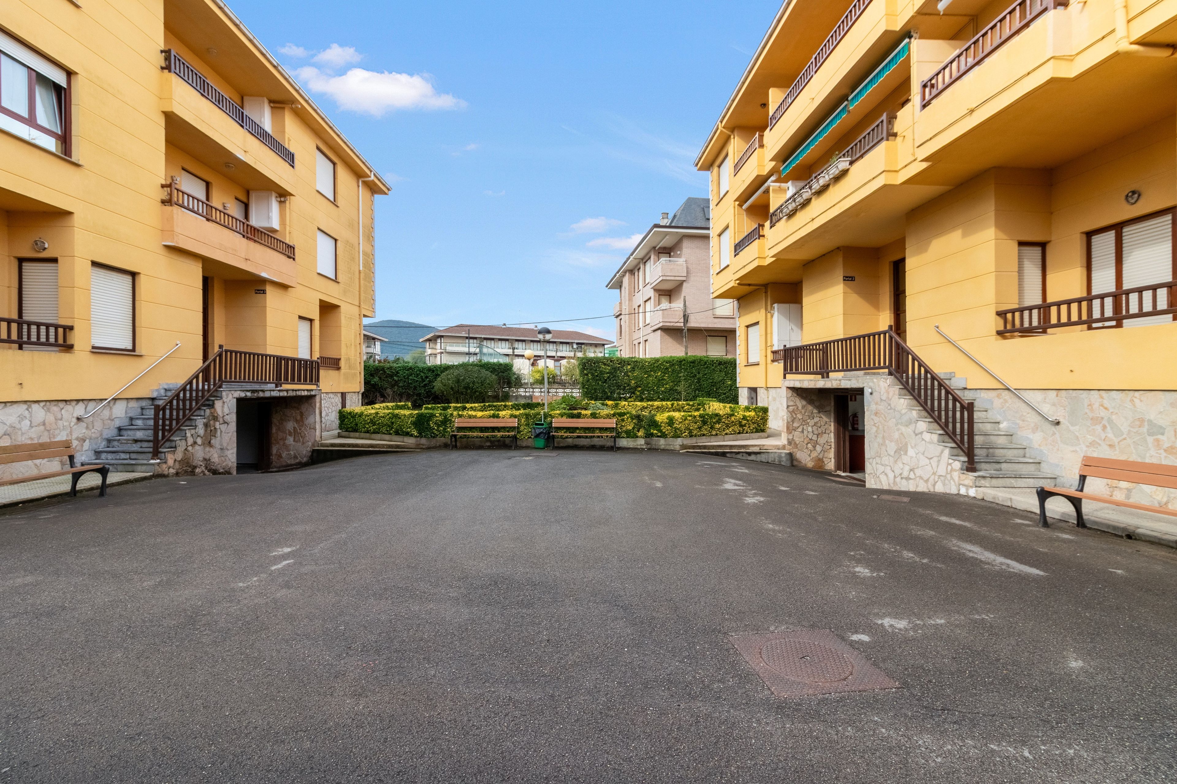 Une cour intérieure avec deux bâtiments jaunes, un espace vert central et un ciel dégagé.
