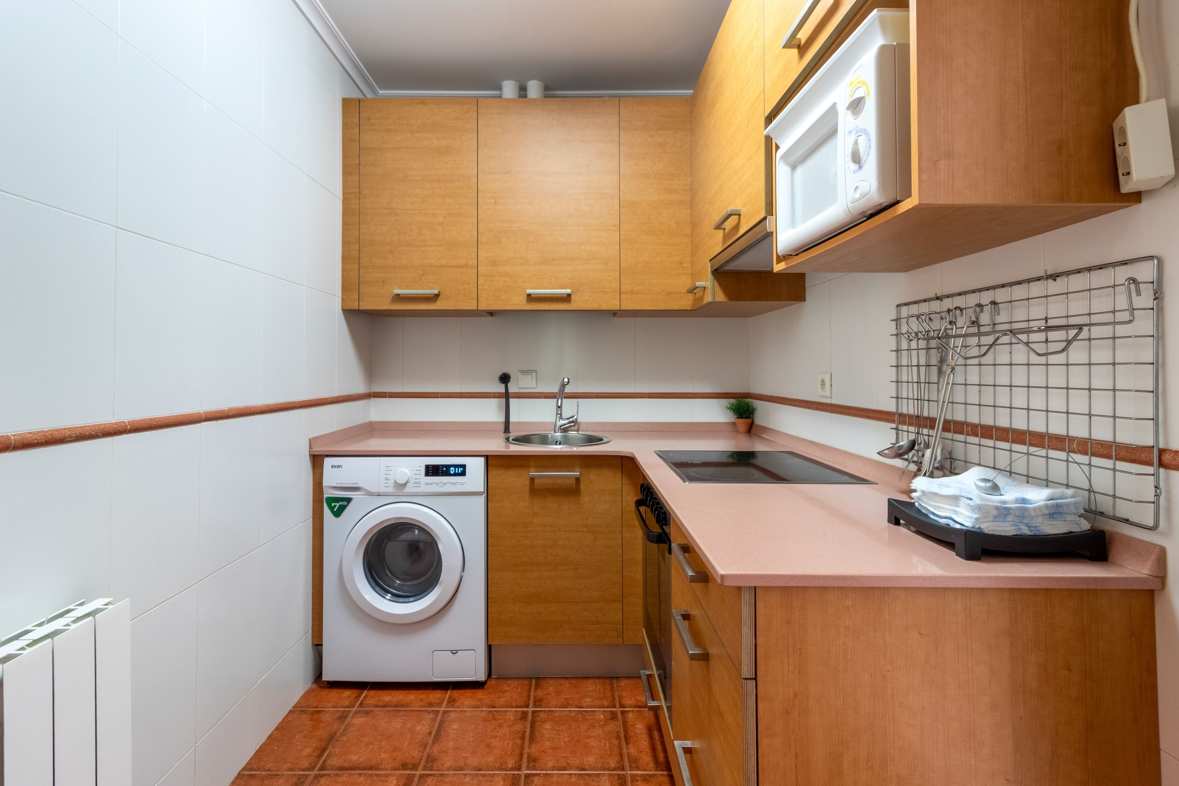 A compact kitchen with wooden cabinets, a built-in washing machine, a sink, and a drying rack.