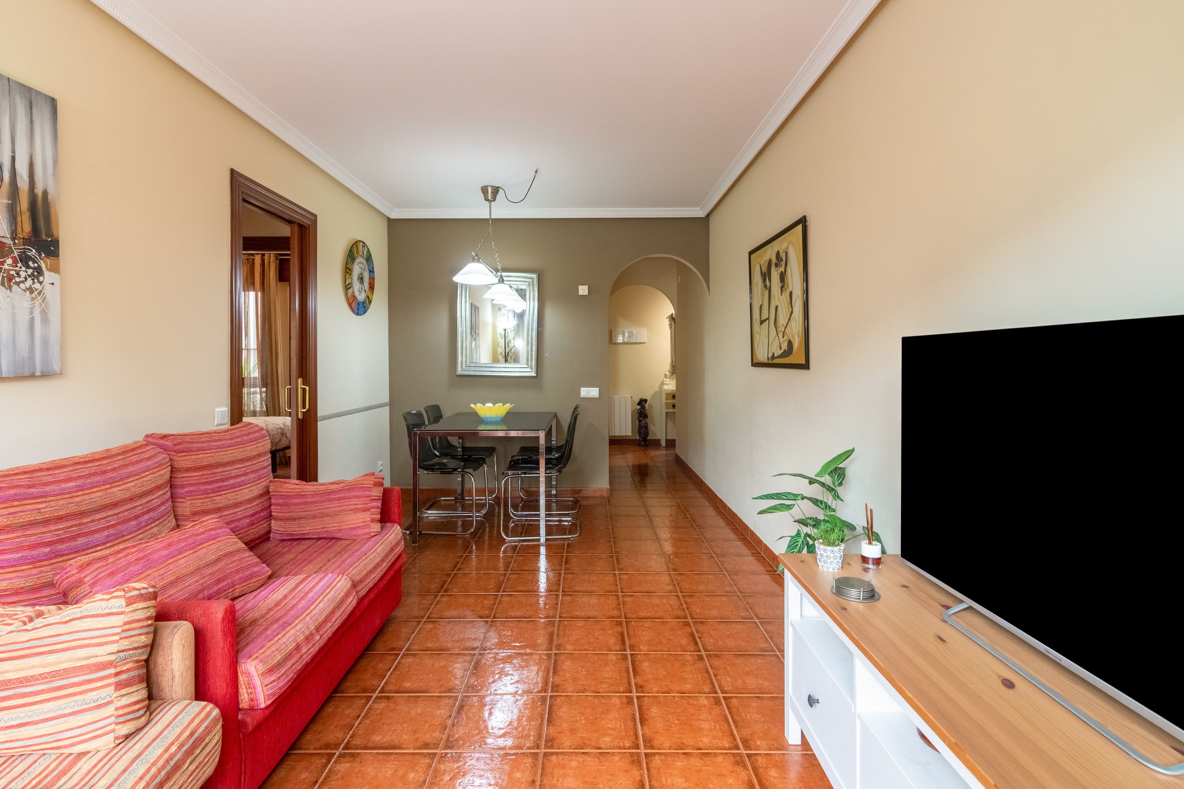 A living room with a sofa, a dining table with chairs, a TV, and a kitchen area with a cabinet.