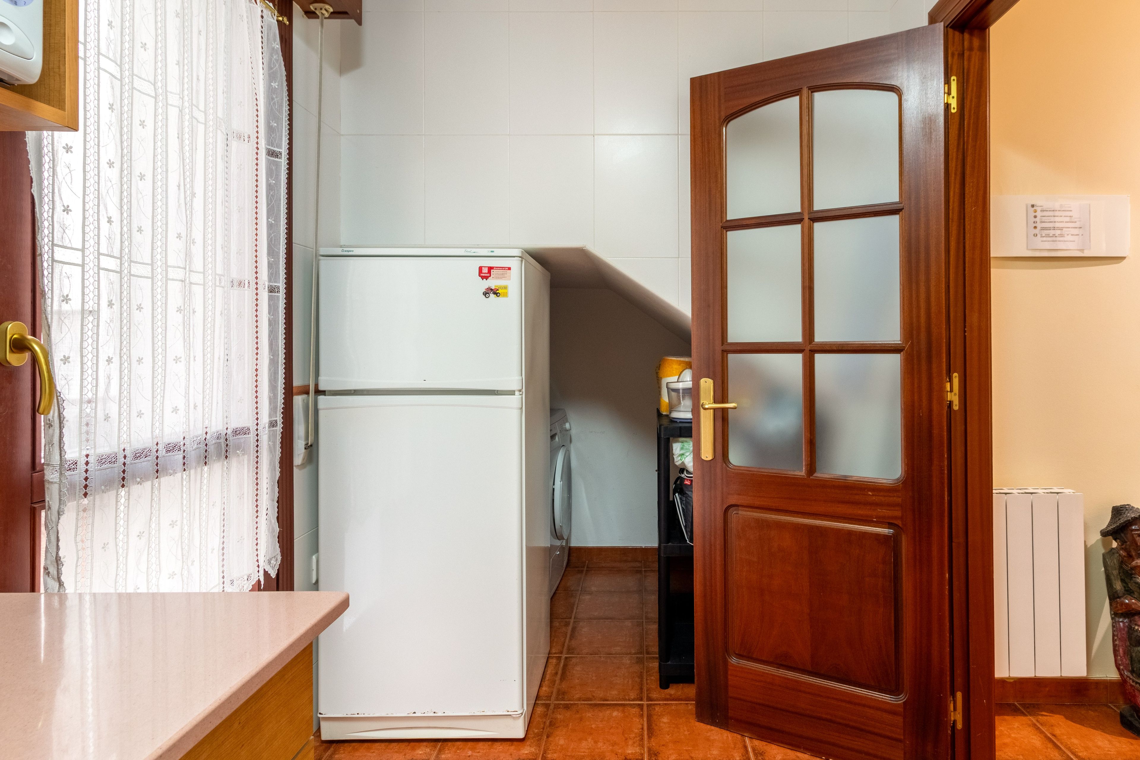 A kitchen with a refrigerator, a wooden door, and a tiled floor.