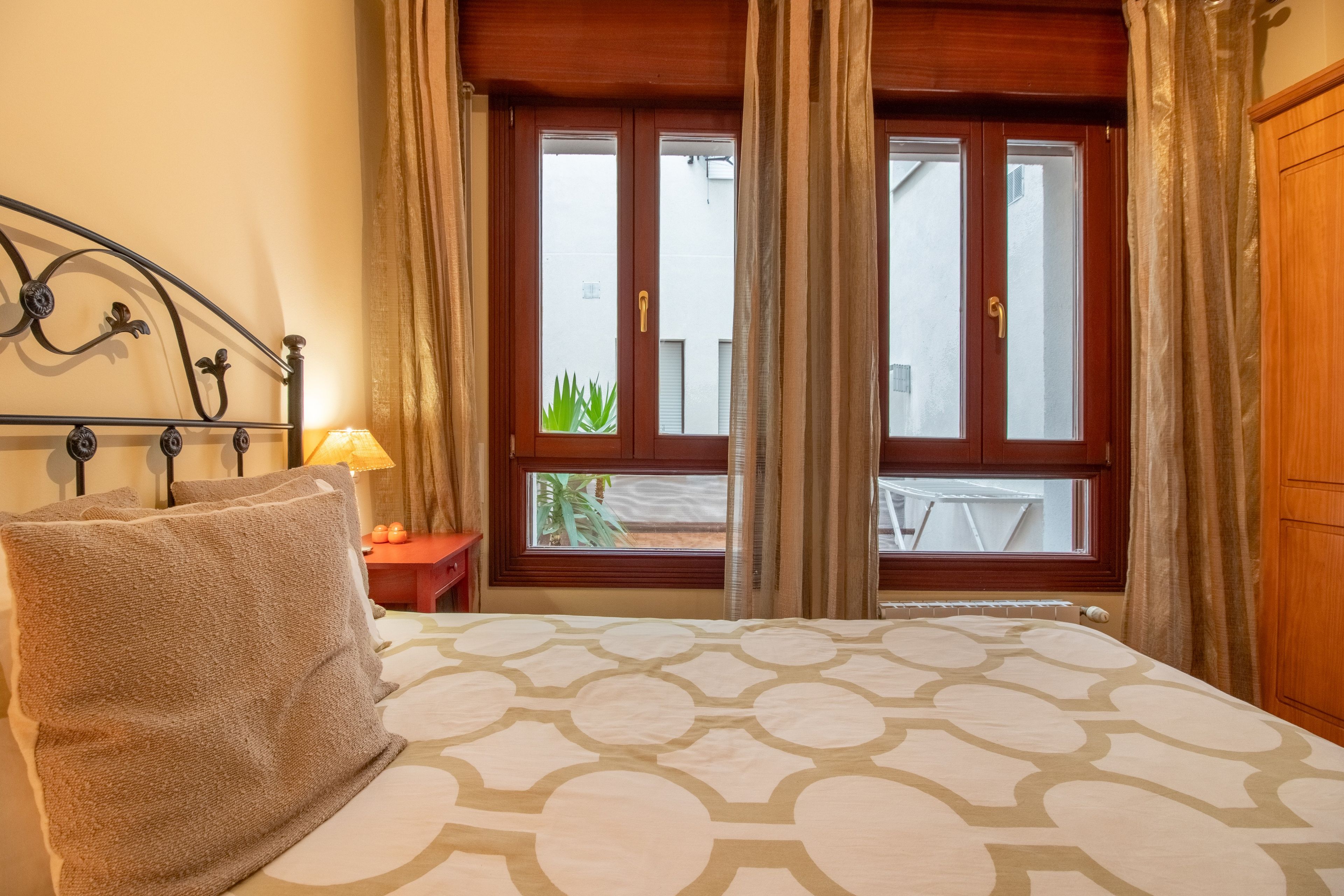 Una camera d'albergo con un letto, una finestra con tende, una lampada da comodino e un asciugamano sul letto.