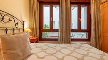 Una camera d'albergo con un letto, una finestra con tende, una lampada da comodino e un asciugamano sul letto.