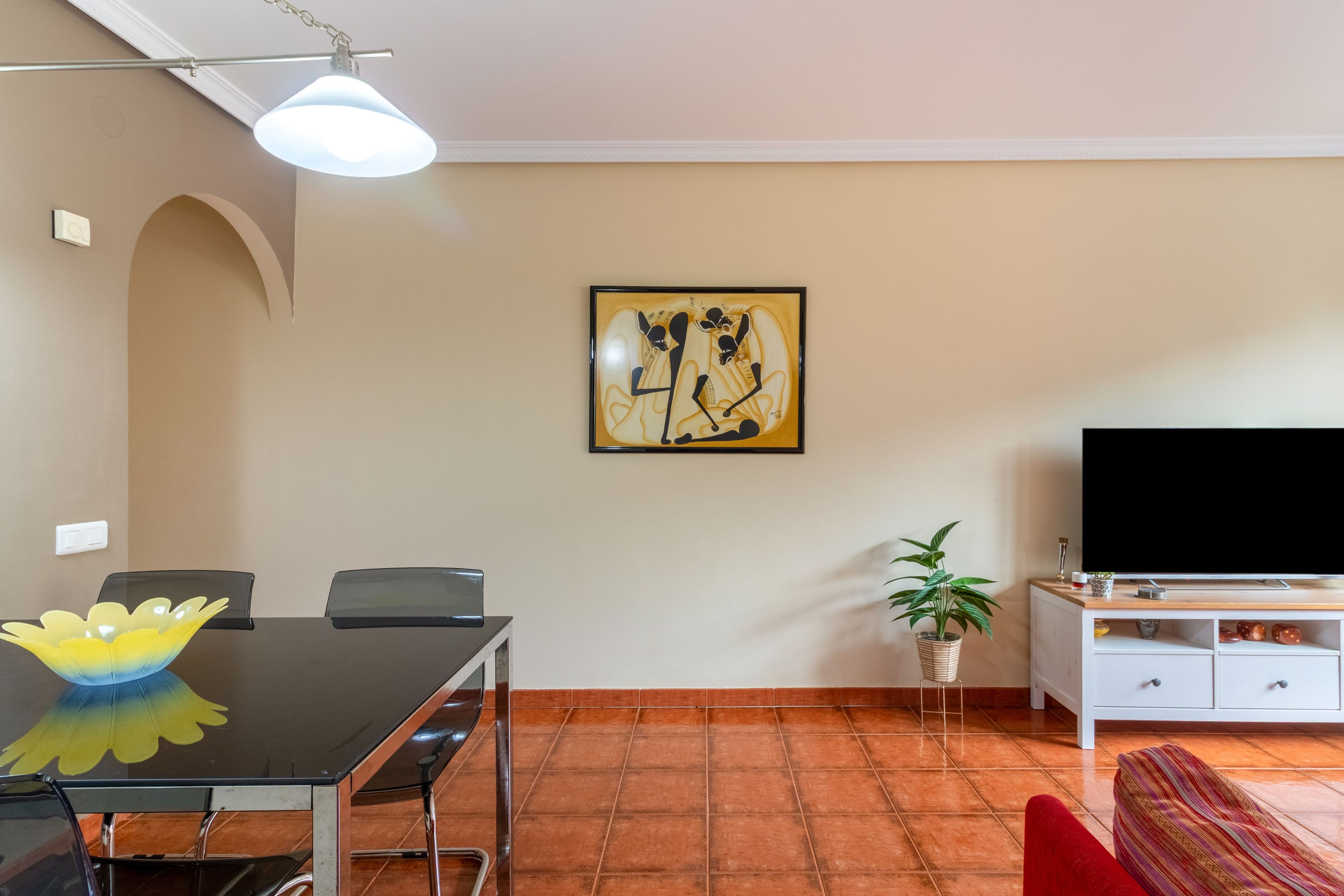 Un soggiorno con tavolo da pranzo, sedie, divano, televisore, un quadro e una pianta.