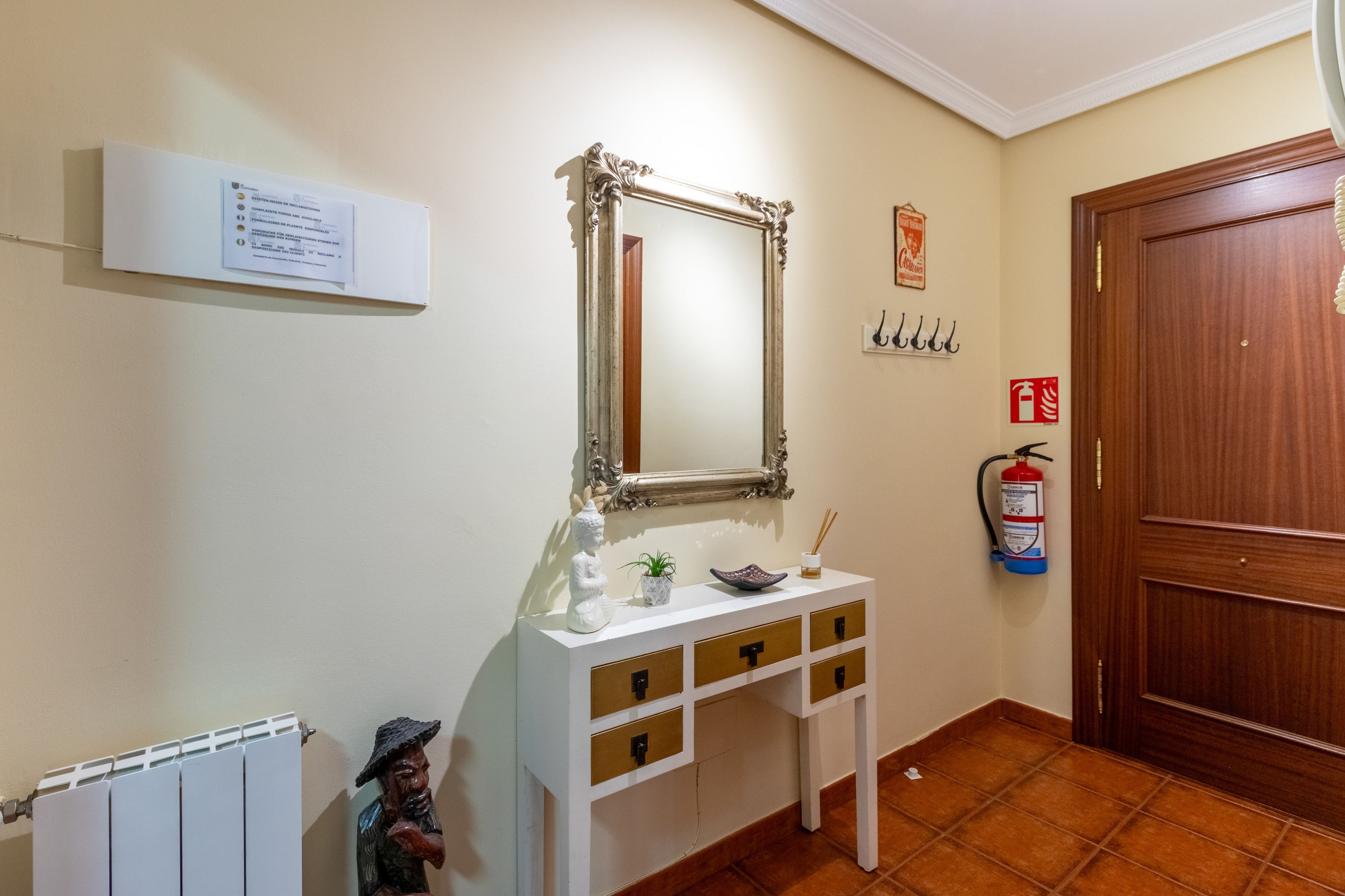 A hallway with a white console table, a mirror, a fire extinguisher, and a door.