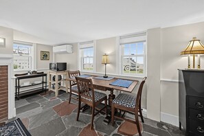 A dining area with a table and chairs, a microwave, a lamp, and a view of the outside. - The Village Anchor/Cozy Flat near Harbor & Shops (Rockport)
