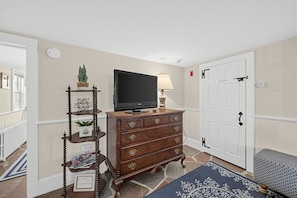 A room with a wooden dresser, a television, a lamp, and a door with a closet. - The Village Anchor/Cozy Flat near Harbor & Shops (Rockport)