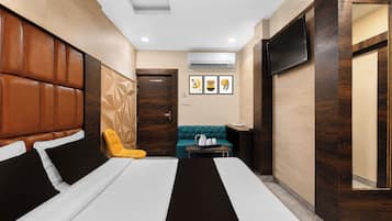 A hotel room with a large bed, a sofa, a small table with a tray, and a TV mounted on the wall.