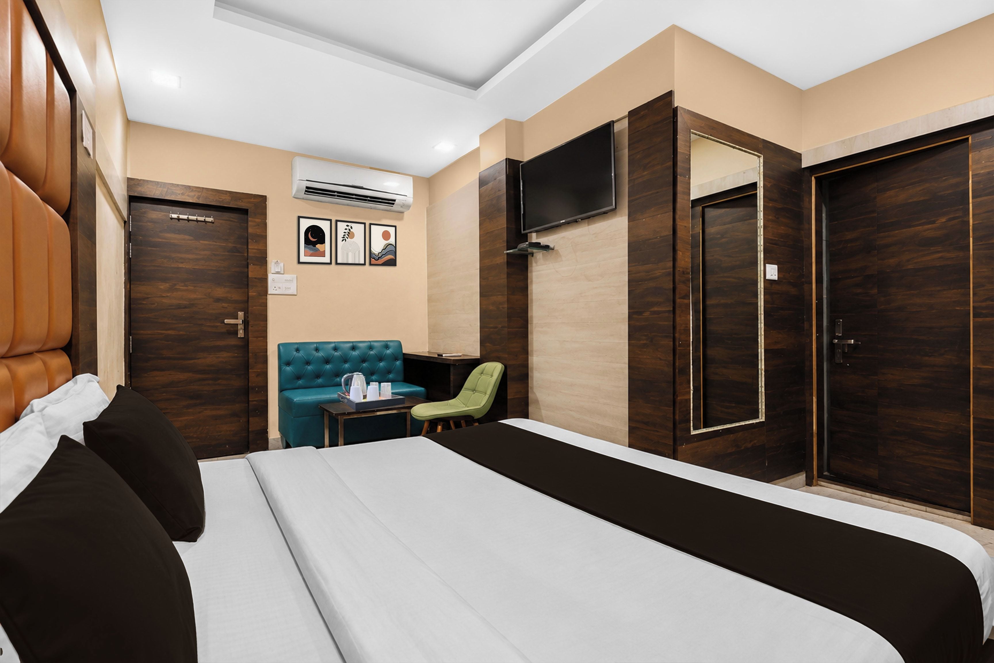 A hotel room with a bed, a seating area with a table, a TV mounted on the wall, and a wardrobe.