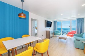 Ein modernes Wohnzimmer mit Essbereich, einem an der Wand befestigten Flachbildfernseher und einem großen Fenster mit Meerblick.